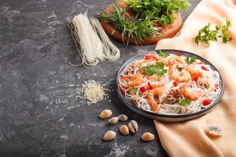 Rice noodles with shrimps or prawns and small octopuses on gray ceramic plate on a black concrete