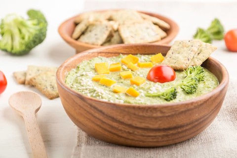 Green broccoli cream soup with crackers and cheese in wooden bowl on a white wooden background and