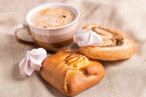 Sweet buns, meringues and coffee cup on a wooden board and linen tablecloth