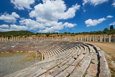 Ancient stadium with rows of seats and wild grass under a cloudy sky, archaeological site, Ancient