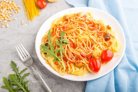 Corn noodles with tomato sauce and arugula on a gray concrete background and blue textile. Side