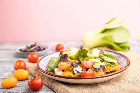 Vegetarian salad of pac choi cabbage, kiwi, tomatoes, kumquat, microgreen sprouts on gray and pink