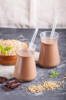 Organic non dairy oats chocolate milk in glass and wooden plate with oats seeds on a black concrete