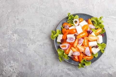 Vegetarian salad with fresh grape tomatoes, feta cheese, lettuce and onion on blue ceramic plate on
