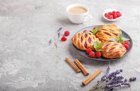 Puff pastry buns with strawberry jam on blue ceramic plate on gray concrete background, cup of