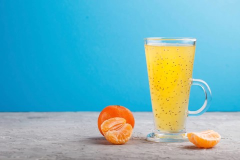 Glass of tangerine orange colored drink with basil seeds on a gray and blue background. Morninig,