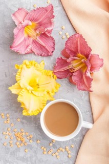 Yellow anf purple day-lilies cup of coffee on a gray concrete background, with orange textile.