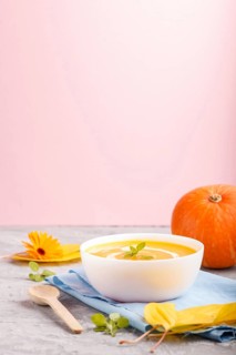 Traditional pumpkin cream soup with in white bowl on a gray and pink background with blue napkin.