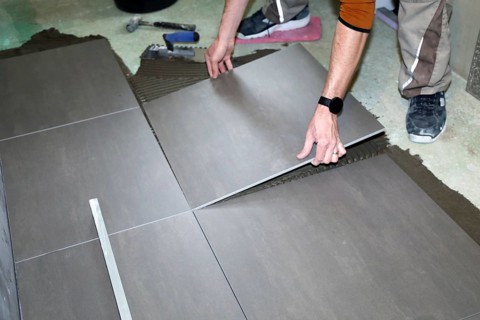 Tiler lays modern large floor tiles in a bathroom