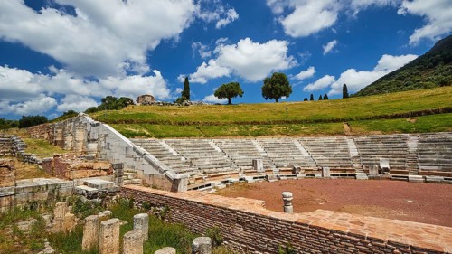 Historic theatre site with tiered rows of seats under a partly cloudy sky, Ancient Theatre,
