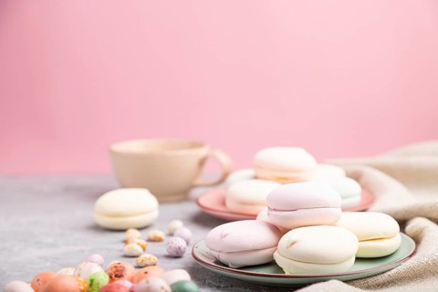 Colored zephyr or marshmallow with cup of coffee and dragees on a gray and pink background and