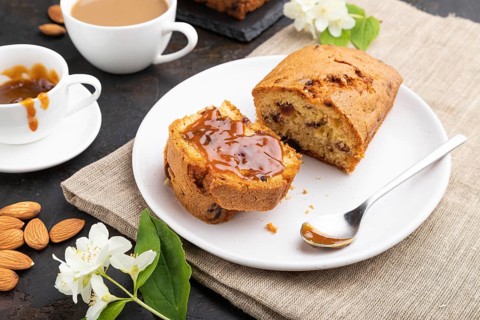 Homemade cake with raisins, almonds, soft caramel and a cup of coffee on a black concrete