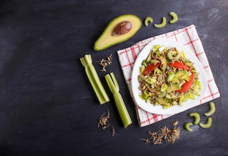 Vegetarian salad of celery, germinated rye, tomatoes and avocado on linen tablecloth, top view,