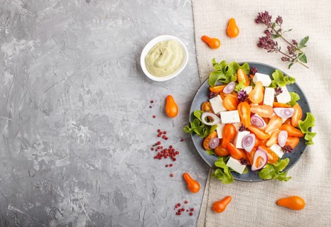 Vegetarian salad with fresh grape tomatoes, feta cheese, lettuce and onion on blue ceramic plate on