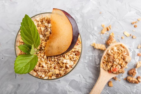 Yoghurt with plum, chia seeds and granola in a glass and wooden spoon on gray concrete background.