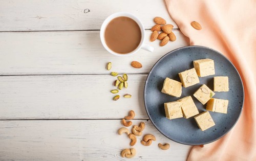 Traditional indian candy soan papdi in a blue ceramic plate with almond, pistache, cashew and a cup