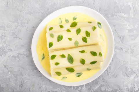 Cannelloni pasta with egg sauce, cream cheese and oregano leaves on a gray concrete background. top