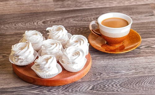 White marshmallows (zephyr) on a round wooden board with cup of coffee on a gray wooden background