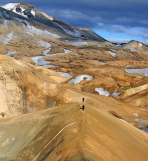 People wander through snow-covered, volcanic landscapes, smoke and vapour drift over brown