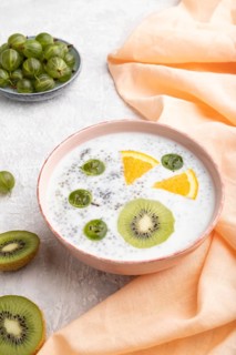 Yogurt with kiwi, gooseberry, chia in ceramic bowl on gray concrete background and orange linen