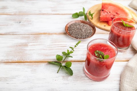 Watermelon juice with chia seeds and mint in glass on a white wooden background with linen textile.