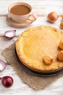 Autumn onion pie and cup of coffee on white wooden background and linen textile. Side view, close