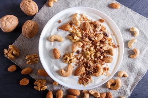 White plate with greek yogurt, granola, almond, cashew, walnuts on black wooden background. top