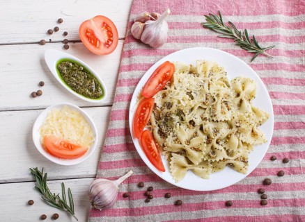 Farfalle pasta with pesto sauce, tomatoes and cheese on a linen tablecloth on white wooden