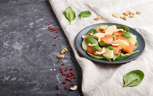 Fresh salmon with pineapple, spinach and cashew on a black concrete background. Side view, copy