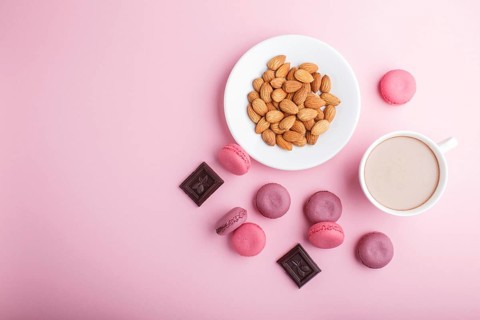 Purple and pink macaron or macaroon cakes with cup of coffee and almonds on pastel pink background.