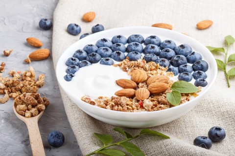Yoghurt with blueberry, granola and almond in white plate with wooden spoon on gray concrete