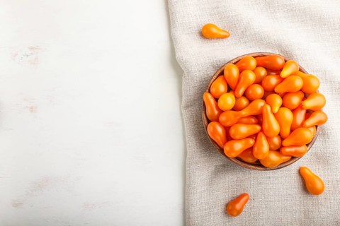 Fresh orange grape tomatoes in wooden bowl on white wooden background with linen napkin. top view,