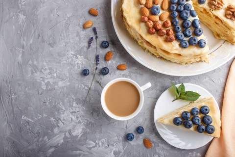 Homemade layered Napoleon cake with milk cream. Decorated with blueberry, almonds, walnuts,