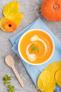Traditional pumpkin cream soup with in white bowl on a gray concrete background with blue napkin.
