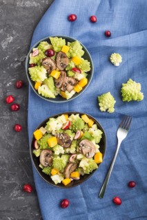 Vegetarian salad from romanesco cabbage, champignons, cranberry, avocado and pumpkin on a black