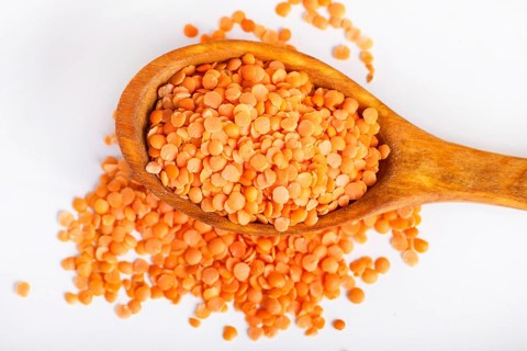 Pile of red lentils in a wooden spoon isolated on white background. Closeup