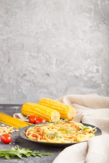 Corn noodles with tomato sauce and arugula on a black concrete background and linen textile. Side
