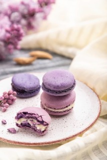 Purple macarons or macaroons cakes with cup of coffee on a gray wooden background and white linen