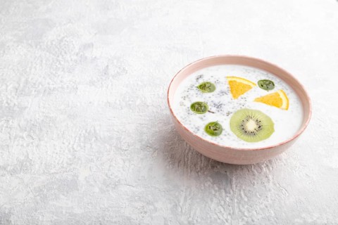 Yogurt with kiwi, gooseberry, chia in ceramic bowl on gray concrete background. Side view, copy