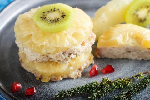 Pieces of baked pork with pineapple, cheese and kiwi on gray plate and blue background, side view,