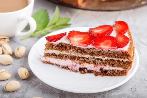 Homemade cake with yoghurt cream, strawberry, pistachio and a cup of coffee on a gray concrete