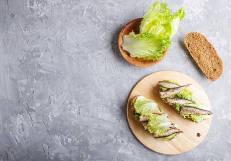 Sprats sandwiches with lettuce and cream cheese on wooden board on a gray concrete background. top