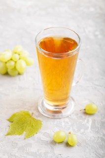 Glass of green grape juice on a gray concrete background. Morninig, spring, healthy drink concept.