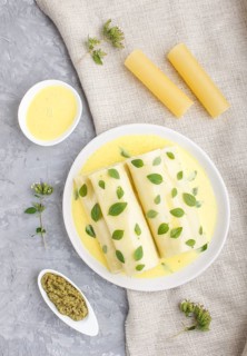 Cannelloni pasta with egg sauce, cream cheese and oregano leaves on a gray concrete background with