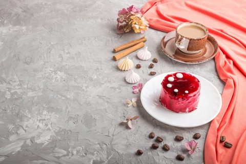 Red cake with souffle cream with cup of coffee on a gray concrete background and red textile. side