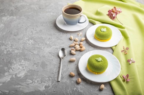 Green mousse cake with pistachio cream and a cup of coffee on a gray concrete background and green