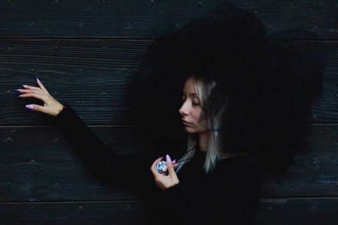 Female white blonde model wear black furry hat leaning by her side against a wooden wall, holding