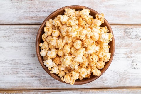Popcorn with caramel in wooden bowl on a white wooden background. Top view, flat lay, close up