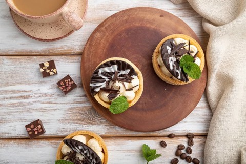 Sweet tartlets with chocolate and cheese cream with cup of coffee on a white wooden background and