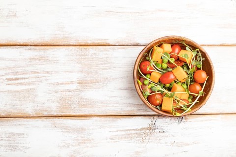 Vegetarian vegetable salad of tomatoes, pumpkin, microgreen pea sprouts on white wooden background.